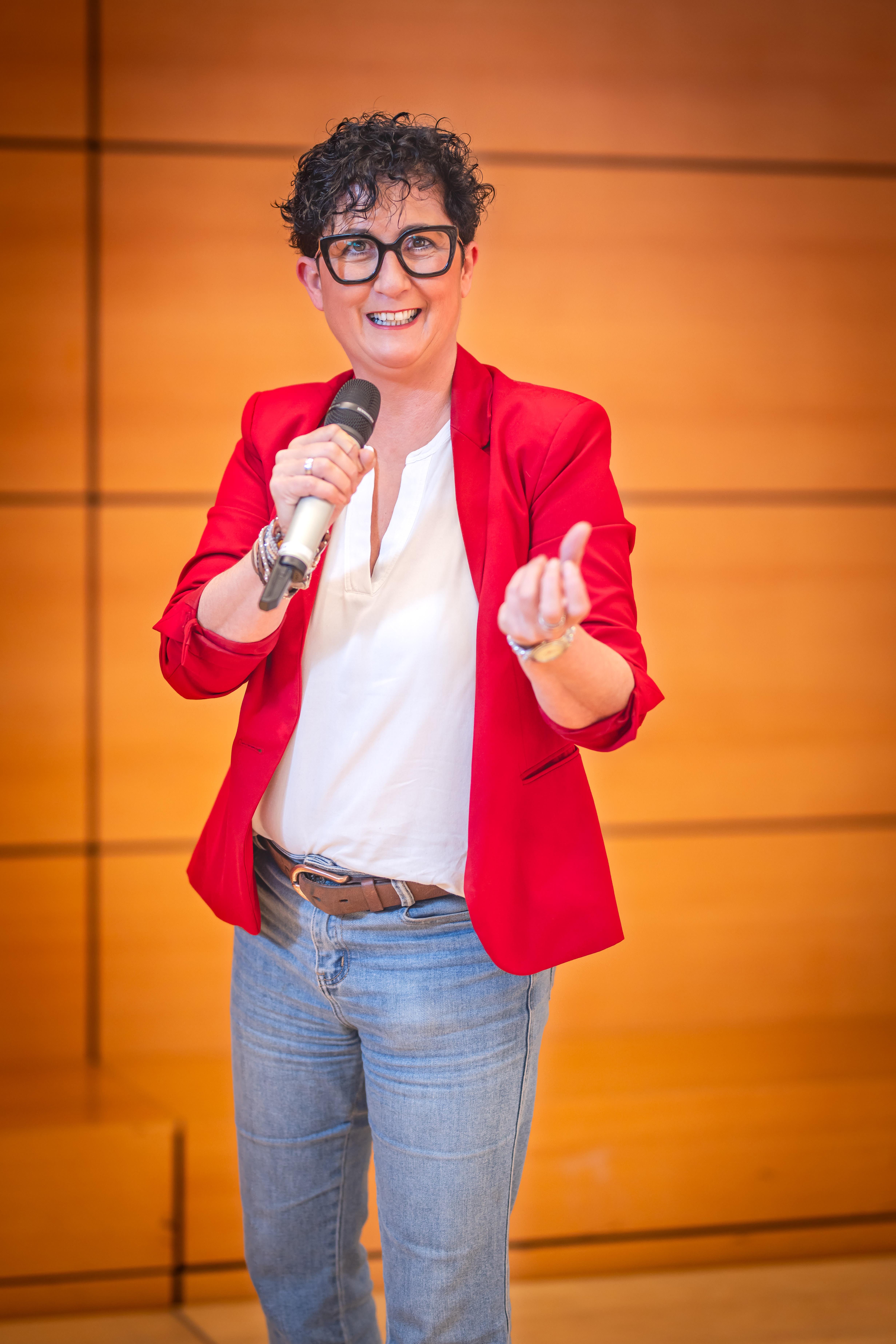 Nicole Mayer im roten Sakko mit schwarzer Brille und Mikrofon